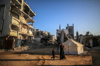 A Palestinian woman carries a child as they walk past the rubble of houses destroyed in previous strikes during the Israeli military offensive, amid the Israel-Hamas conflict, in Deir el-Balah, Gaza Strip, on November 13, 2024.