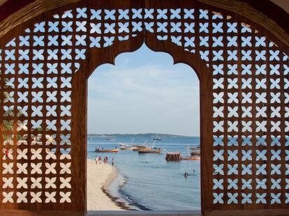 A view of Stonetown beach and bay through a lattice work window of a hotel in Zanzibar, Tanzania