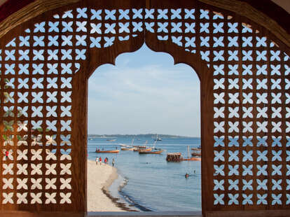 A view of Stonetown beach and bay through a lattice work window of a hotel in Zanzibar, Tanzania