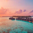 Aerial sunset panoramic landscape luxury tropical resort water villas. Beautiful island beach orange sunrise sea sky. Amazing bird eyes panorama Maldives paradise tropical bay.