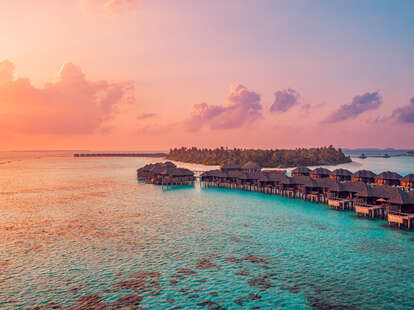 Aerial sunset panoramic landscape luxury tropical resort water villas. Beautiful island beach orange sunrise sea sky. Amazing bird eyes panorama Maldives paradise tropical bay.