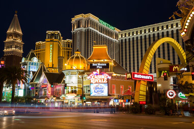 A nighttime photo of the Las Vegas Strip shows fast food chain, luxurious hotels, and a variety of other businesses aglow with their illuminated signage.