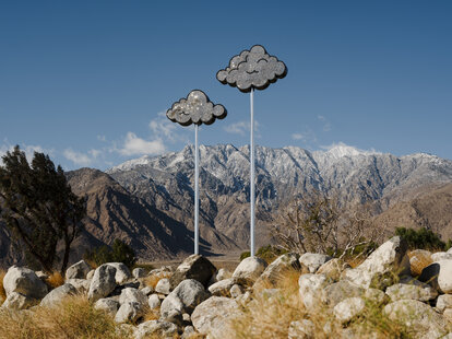 art installation of two clouds on tall poles in front of dramatic mountain backdrop for desert x art show in palm springs