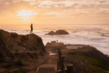 sunset over the coast of san francisco, california, where a woman stands on a rock admiring the pacific ocean