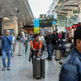 A person in a brightly colored shirt pushes a suitcase along a train station as the surrounding crowd moves around them.