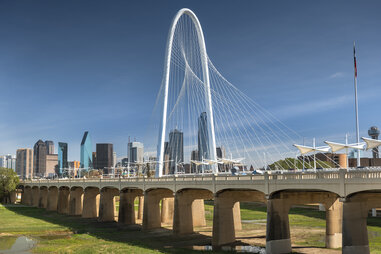 margaret Hunt Hill Bridge over the Trinity River in Dallas, Texas in the daytime with the downtown dallas skyline behind it