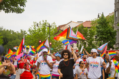 A crowd of Pride celebrators wave miniature Pride flags while wearing rainbow-hued clothing.