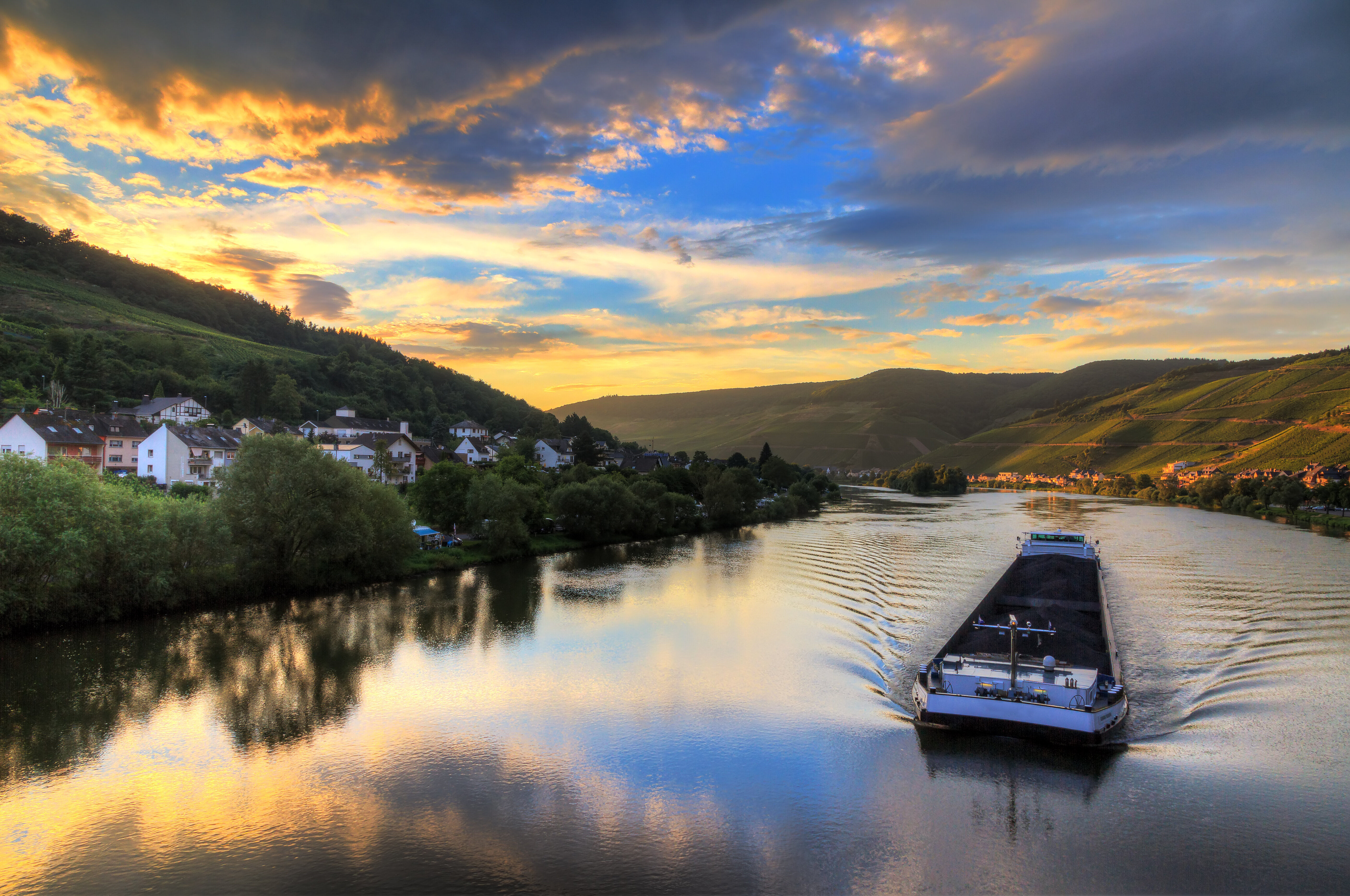 Beautiful vibrant sunset view of the river Moselle at the small wine growing town Zell (an der Mosel) with hills full of grape vines with a barge on the river