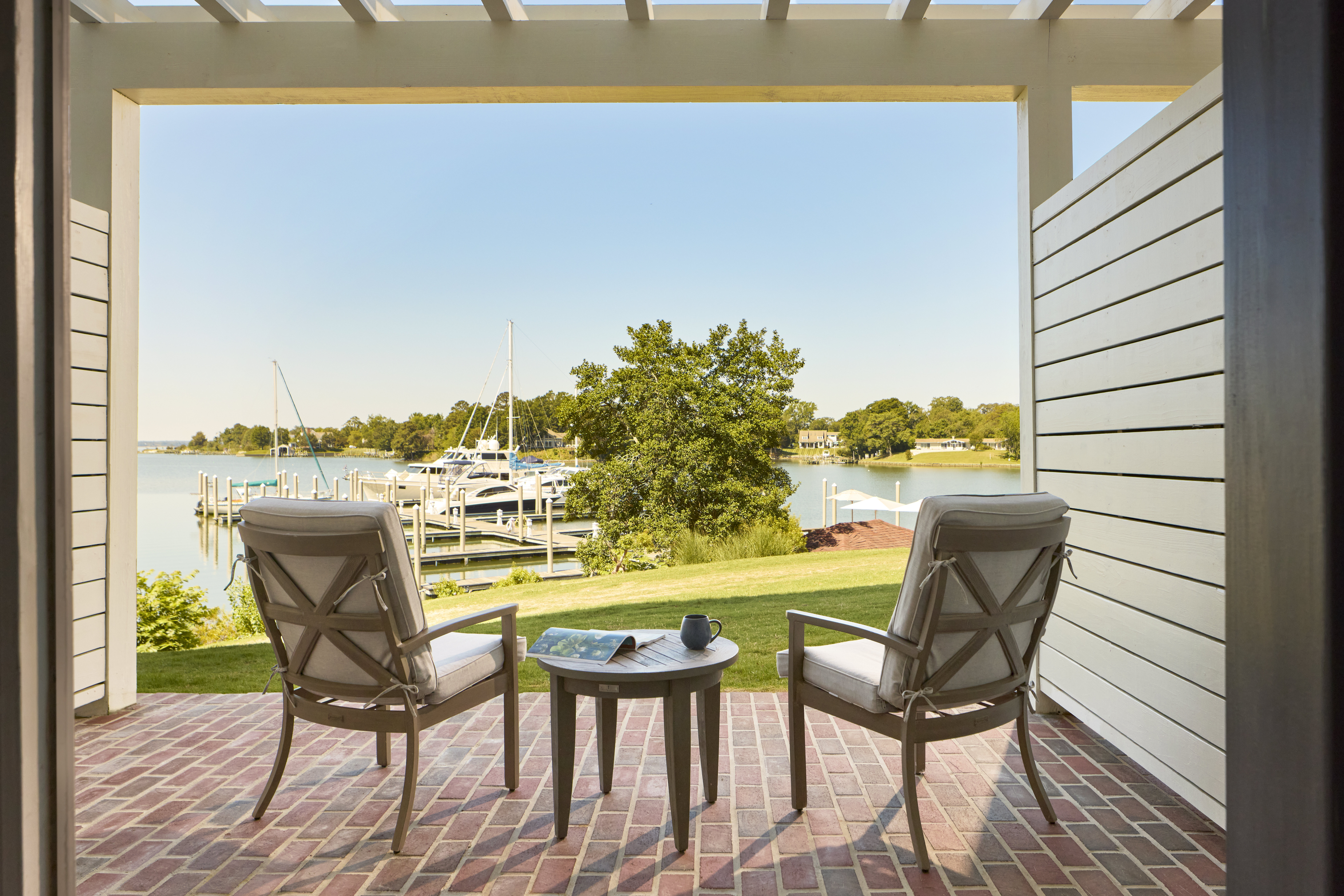 a pair of chairs with a coffee table on the deck overlooking a dock and the chesapeake bay at the tides inn