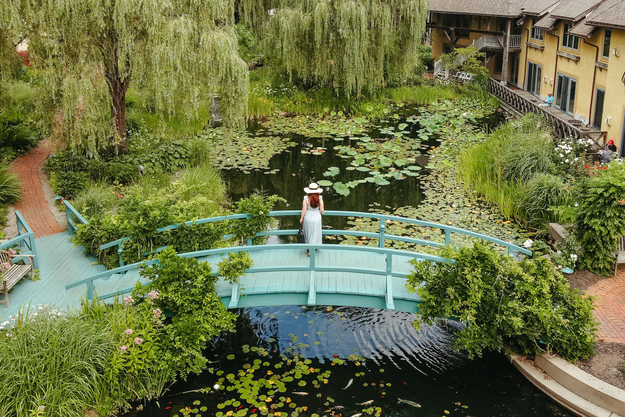 a woman on a turquoise bridge looking into the verdant pond at Mirbeau Inn & Spa in new york