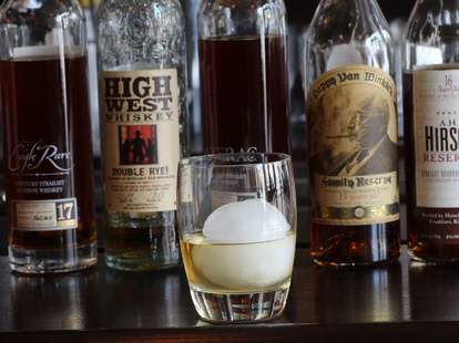 Close up of whiskey bottles and a glass filled with whiskey.