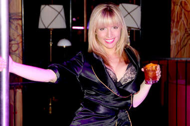 A bartender at Ivan Kane's Royal Jelly models on a pole while holding a cocktail