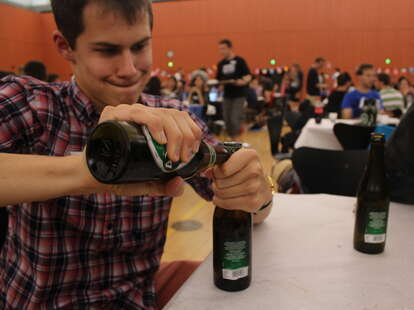 a guy using a beer bottle to open another beer bottle