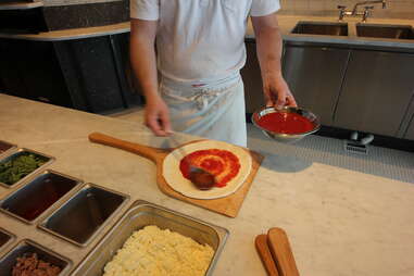 putting red sauce on a pizza at Pizzeria Locale Denver