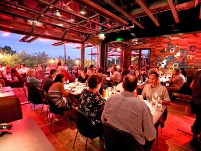People dining in the dimly lit interior of Root Down with open windows and a view of downtown.