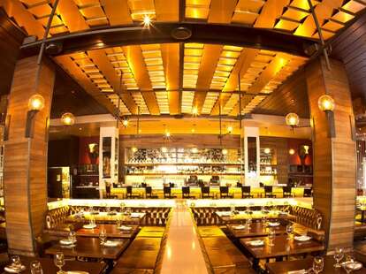 Panoramic of the inside of Tavernita, long tables and a bar in the back, decorated in gold and yellow.