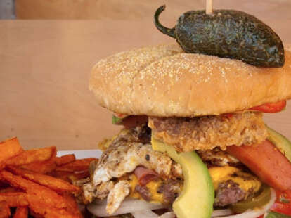 A burger piled high with avocado, peppers and jalapenos.
