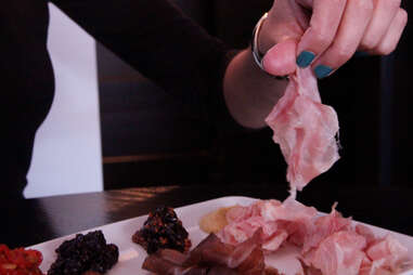 Fingers picking up a piece of Benton's ham at a.bar