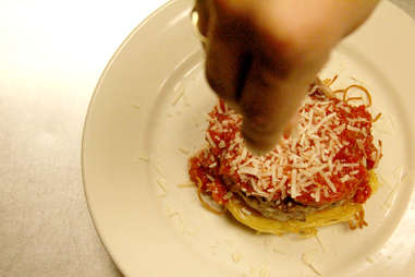 Sprinkling parmesan cheese atop PYT's Spaghetti Burger