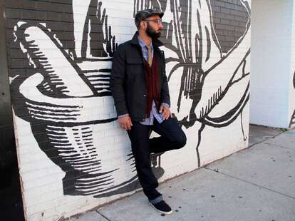 A stylish man leans against a graffiti wall.